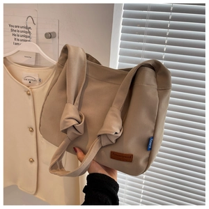 Detail view of beige canvas tote bag with knot strap design and leather logo patch