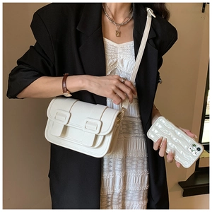 Close-up of a white textured faux leather crossbody bag with metallic buckles