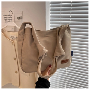 Close-up of beige canvas tote bag featuring a knotted shoulder strap and leather logo patch