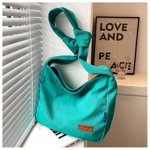 Detail of teal canvas bucket bag featuring knotted shoulder strap and leather logo patch