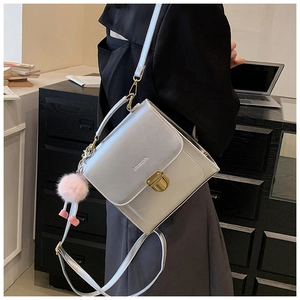 Schicke silberne Umhängetasche mit Goldschließe und rosa Plüsch-Anhänger am Model
