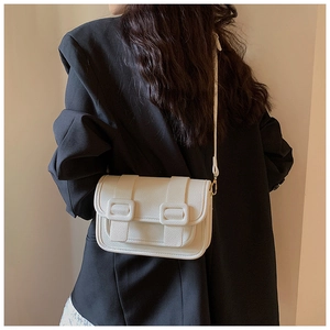 Detail of white lychee leather crossbody bag on black suit showing texture and strap