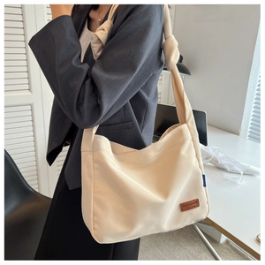 Detail of cream canvas tote bag featuring brown leather logo patch and knotted shoulder strap