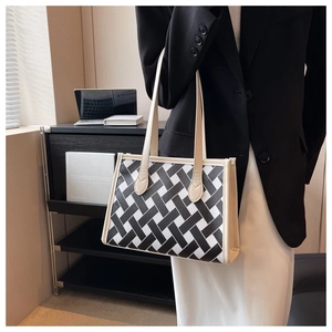 Detail of checkered woven tote bag with cream leather handles held by a model