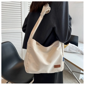 Detail of knot shoulder strap and brown leather logo on minimalist beige canvas tote bag