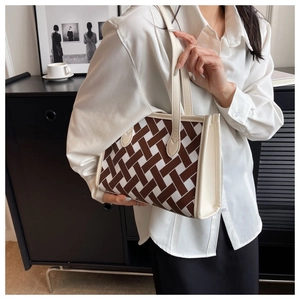 Close-up of woven tote bag with brown geometric pattern and cream leather handles