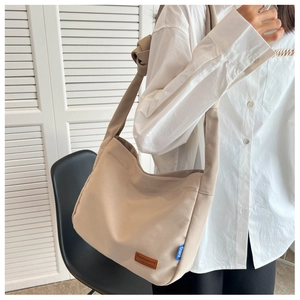 Detail of khaki canvas tote bag featuring brown leather logo tag and wide knotted strap