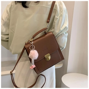 Detail der braunen Ledertasche mit goldenem Verschluss und süßem rosa Plüschanhänger