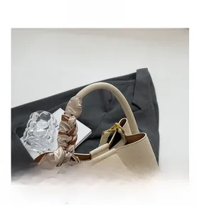 Dettaglio del manico della borsa a secchiello in pelle crema con foulard di seta a cuori