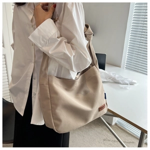 Detailed view of a beige canvas tote bag worn cross-body showing its texture and strap