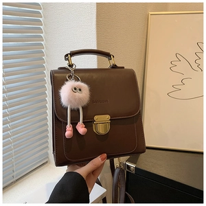 Detail der dunkelbraunen matten Ledertasche mit Metallschnalle und rosa Plüschanhänger