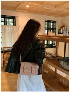 Detail of pink pebbled leather crossbody bag with dual square buckles on a shoulder strap