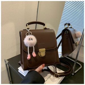 Detail eines dunkelbraunen Lederrucksacks mit goldenem Schloss und rosa Plüschanhänger