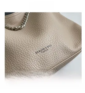 Dettaglio borsa in pelle beige martellata con catena in metallo argento e logo impresso
