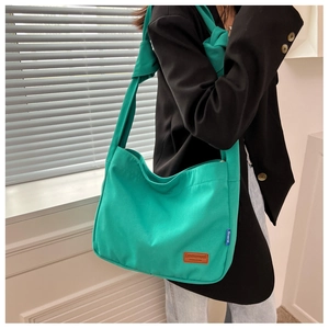 Detail of green canvas bucket bag with a knotted shoulder strap and leather brand label