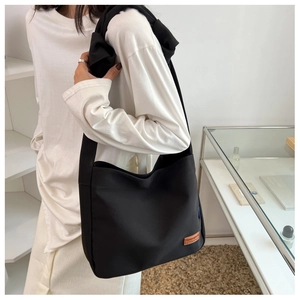 Detail of black canvas tote bag showing wide knotted shoulder strap and leather logo patch