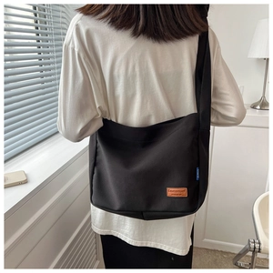 Detail of black canvas messenger bag with brown leather patch and wide shoulder strap