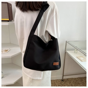Close-up of black canvas tote bag featuring brown leather logo patch and wide strap