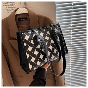 Detail of black and white woven tote bag featuring leather handles in a chic urban setting