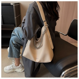Dettaglio della borsa tote beige texture litchi con catena d'argento indossata da modella