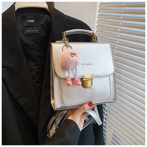 Detail einer silbernen quadratischen Tasche mit rosa Plüschmonster-Anhänger am Modell