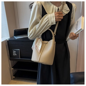 Dettaglio borsa a secchiello in pelle beige con sciarpa a cuori sul manico