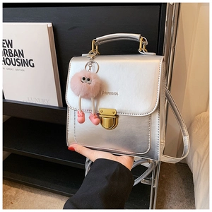 Detail der silbernen Metallic-Mini-Handtasche mit goldener Schnalle und Plüschanhänger