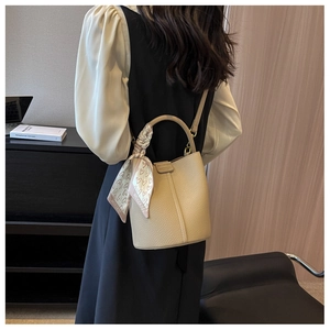 Dettaglio borsa a secchiello beige con trama litchi, foulard in seta e fibbie in metallo