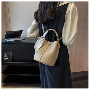 Dettaglio della borsa a secchiello in pelle beige con foulard decorativo sul manico