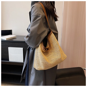 Detail of large woven straw shoulder bag with brown leather trim worn by a model
