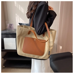 Detail of canvas tote bag featuring premium leather handles and side brand label