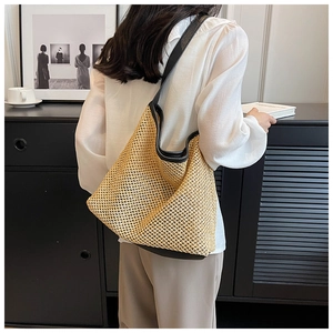 Detailed view of large straw tote bag with black leather straps on model's shoulder