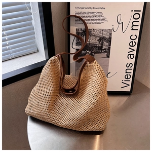 Detail of hand-woven straw tote with brown leather strap on a minimalist metal table