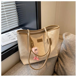 Detail of checkered woven tote bag featuring a leather logo and cute plush monster charm