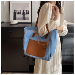 Detail of light blue canvas tote bag with brown leather pocket and long shoulder straps