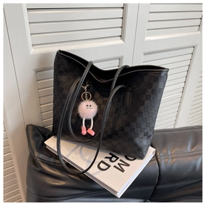 Detail of black checkered tote bag with pink plush charm on leather sofa