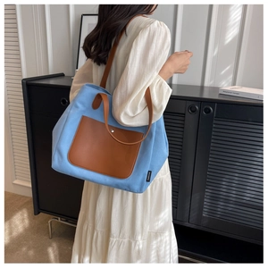 Detail of light blue canvas tote bag with brown leather handles and outer pocket