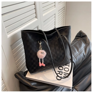 Detail of black checkered tote bag with pink plush monster charm on leather bench
