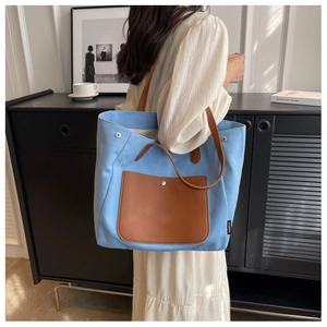 Detail of blue canvas tote bag with leather pocket and shoulder strap on model