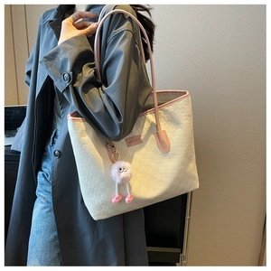 Detail of white woven tote bag with pink leather trim and monster charm pendant