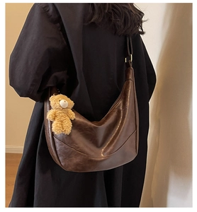 Detail of dark brown hobo bag with vintage texture and cute plush bear charm accessory