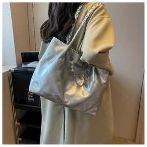 Detail of silver quilted tote bag with woven strap and pearl chain charm shown on model