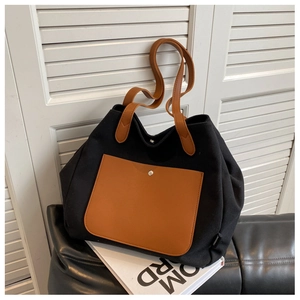 Close-up of black canvas tote bag featuring brown leather pocket and metal snap button