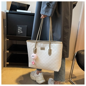 Detail of checkered embossed beige tote bag featuring a pink plush charm and metal tag