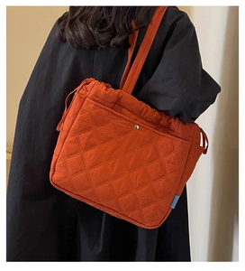 Détail du sac cabas matelassé orange avec cordon de serrage et étiquette bleue sur manteau noir