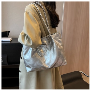 Close-up of silver quilted tote bag with pearl chain detail worn by model with trench coat