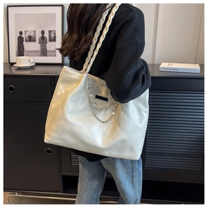 Detail of cream quilted tote bag featuring woven rope strap and pearl chain charm