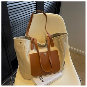 Detail of canvas tote bag showing dark brown leather handles and reinforced metal rivets