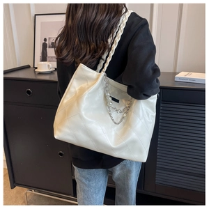 Detail of white quilted tote bag featuring pearl chain accents and woven shoulder strap
