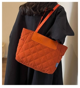 Quilted orange tote bag detail with diamond stitching and leather logo patch on black coat